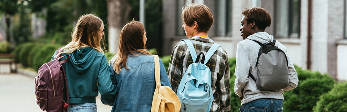 Back view of multiethnic teenagers with backpacks walking together on street